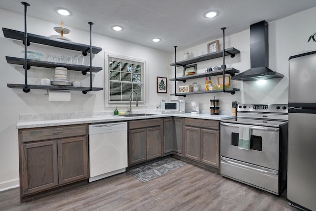 kitchen featuring sink, wall chimney exhaust hood, light stone countertops, appliances with stainless steel finishes, and wood-type flooring