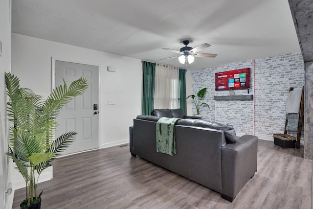 living room with hardwood / wood-style floors, ceiling fan, and brick wall