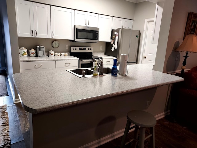 kitchen with dark hardwood / wood-style floors, an island with sink, a breakfast bar, white cabinets, and appliances with stainless steel finishes