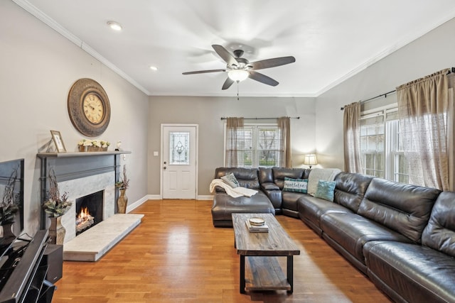 living room with a fireplace, light wood-type flooring, ceiling fan, and ornamental molding