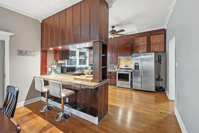 kitchen featuring kitchen peninsula, crown molding, a breakfast bar area, exhaust hood, and appliances with stainless steel finishes