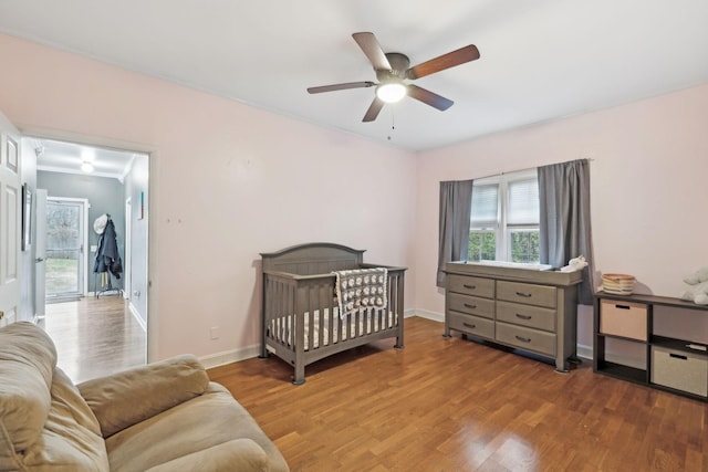 bedroom with hardwood / wood-style flooring, a nursery area, and ceiling fan