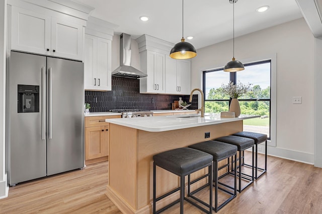 kitchen with stainless steel fridge, wall chimney exhaust hood, sink, white cabinetry, and an island with sink