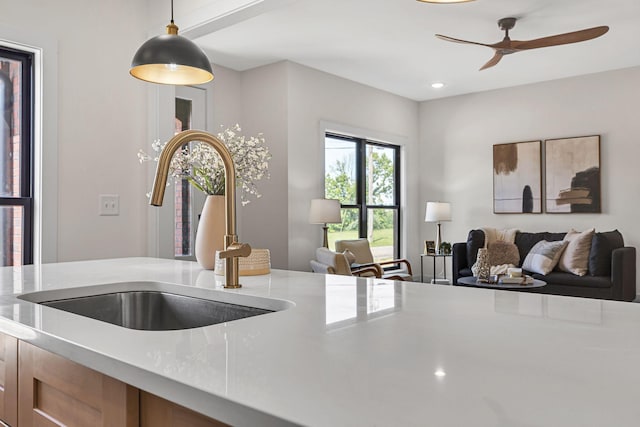 kitchen with light stone counters, sink, ceiling fan, and decorative light fixtures