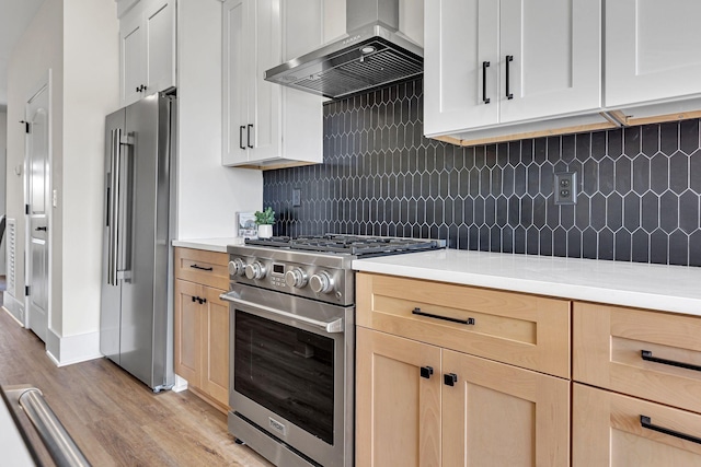 kitchen featuring decorative backsplash, light brown cabinetry, premium appliances, wall chimney range hood, and white cabinets