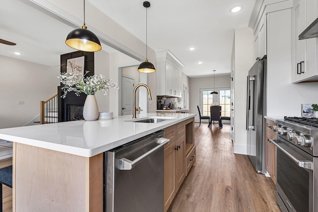 kitchen featuring premium appliances, sink, white cabinets, hanging light fixtures, and a large island