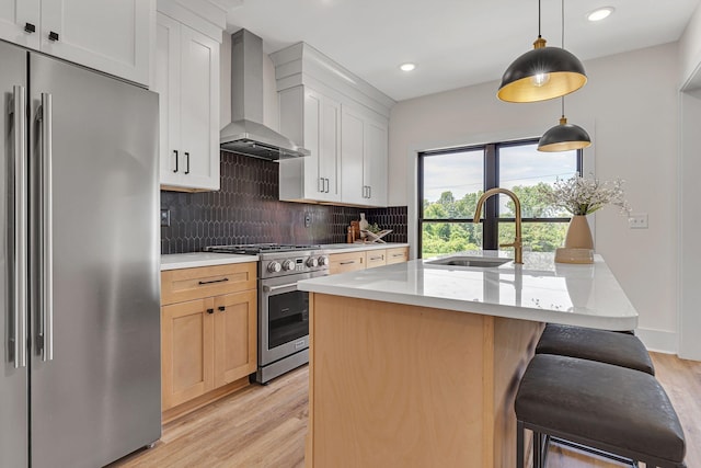 kitchen featuring premium appliances, sink, wall chimney range hood, a center island with sink, and white cabinetry