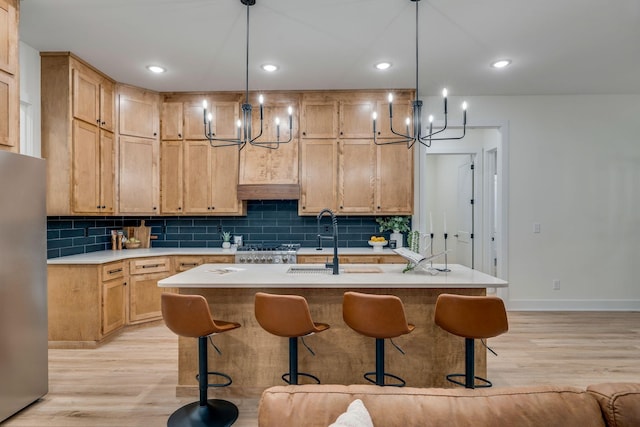 kitchen with decorative light fixtures, light hardwood / wood-style floors, an island with sink, and stainless steel refrigerator