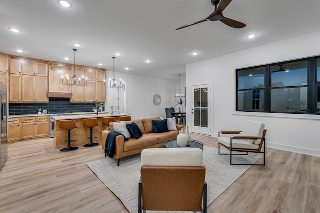 living room featuring ceiling fan with notable chandelier and light wood-type flooring