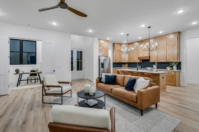 living room featuring ceiling fan with notable chandelier and light wood-type flooring