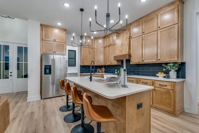 kitchen featuring hanging light fixtures, a kitchen island with sink, stainless steel fridge with ice dispenser, light hardwood / wood-style floors, and decorative backsplash