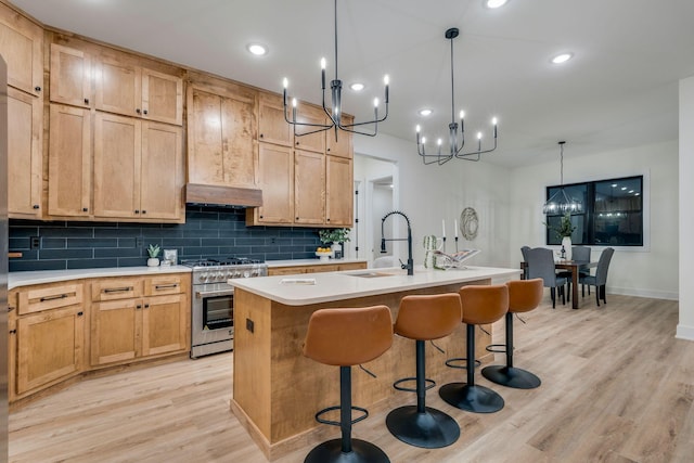 kitchen featuring tasteful backsplash, high end stove, sink, decorative light fixtures, and an island with sink