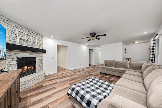 living room with a stone fireplace, ceiling fan, and wood-type flooring