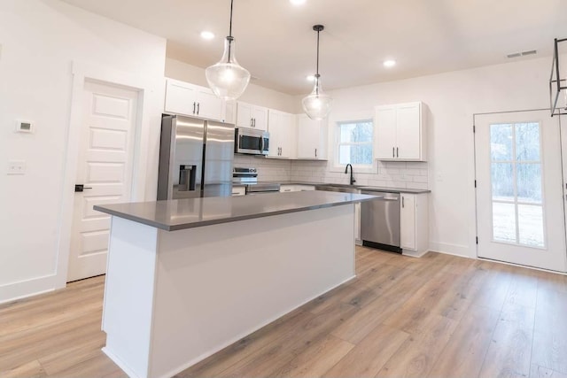 kitchen with appliances with stainless steel finishes, white cabinetry, hanging light fixtures, and a kitchen island