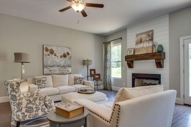 living room with a fireplace, ceiling fan, and dark wood-type flooring