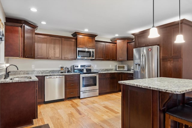 kitchen featuring a kitchen bar, stainless steel appliances, sink, light hardwood / wood-style flooring, and hanging light fixtures