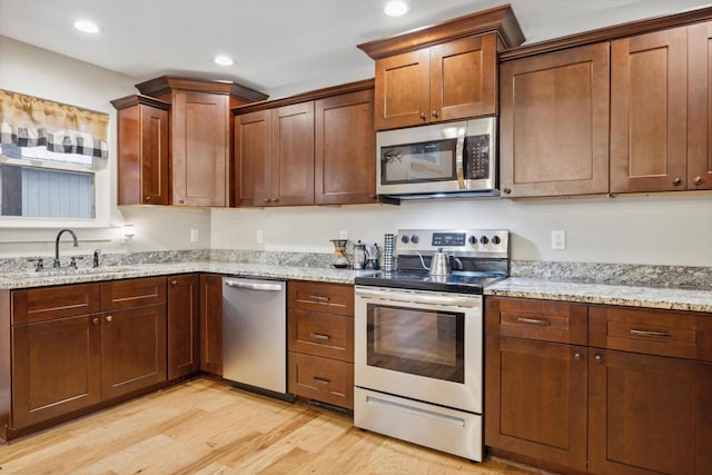 kitchen featuring sink, light stone counters, light wood-type flooring, and stainless steel appliances