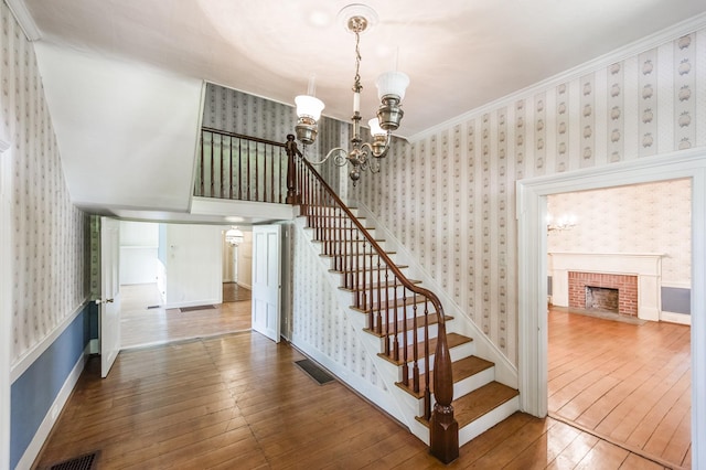 staircase with a fireplace, hardwood / wood-style floors, an inviting chandelier, and ornamental molding