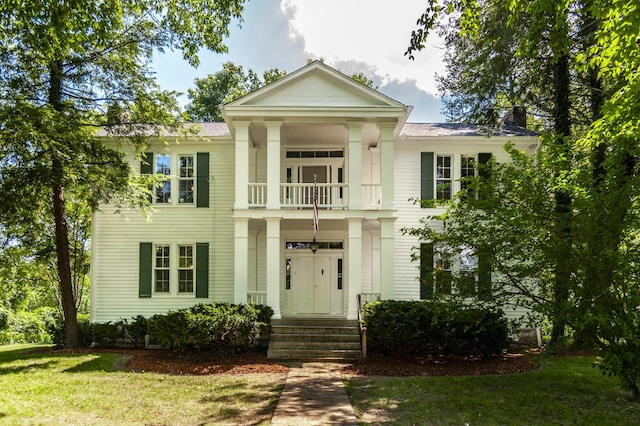 greek revival house featuring a balcony and a front yard