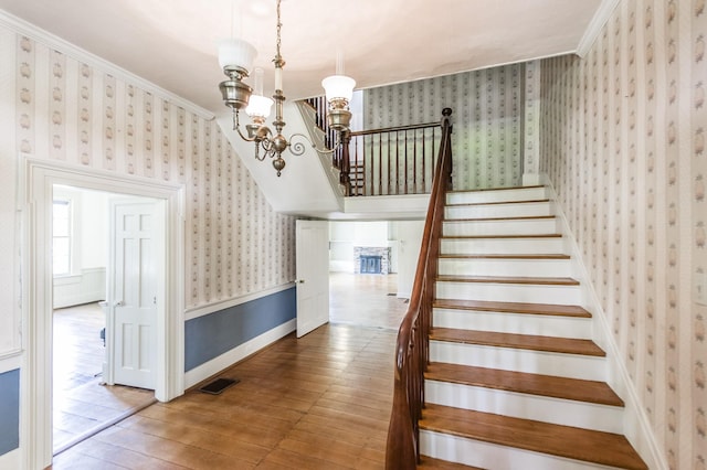 stairway with hardwood / wood-style floors, a notable chandelier, and ornamental molding