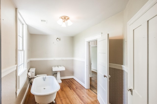 bathroom with hardwood / wood-style flooring, a bathing tub, toilet, and a wealth of natural light