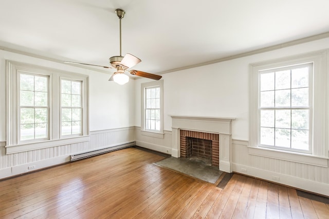 unfurnished living room with a brick fireplace, baseboard heating, crown molding, ceiling fan, and hardwood / wood-style floors