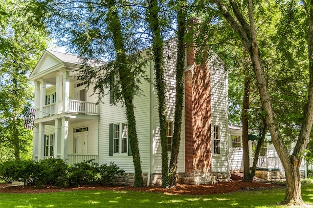 greek revival inspired property featuring a balcony and a front yard