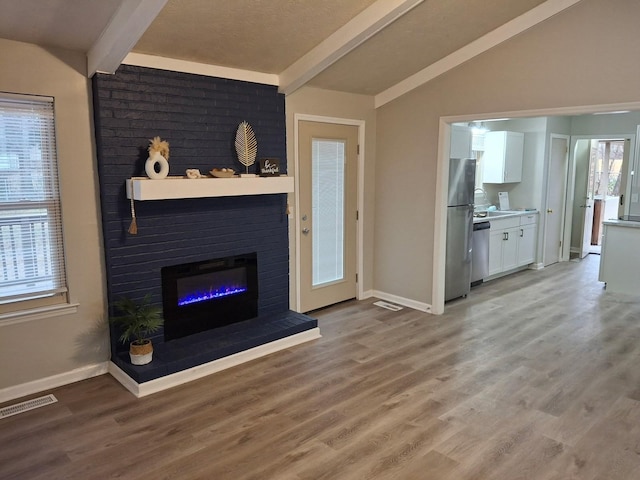 unfurnished living room featuring lofted ceiling with beams, a brick fireplace, and hardwood / wood-style floors