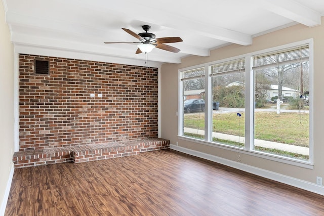 empty room featuring ceiling fan, dark hardwood / wood-style flooring, beamed ceiling, and brick wall