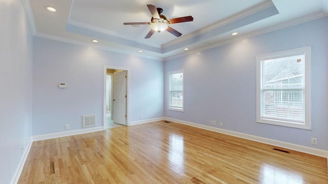 empty room with light wood-style flooring, visible vents, a raised ceiling, and crown molding