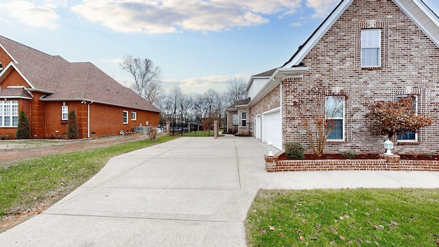 view of side of property with an attached garage, brick siding, fence, a yard, and concrete driveway