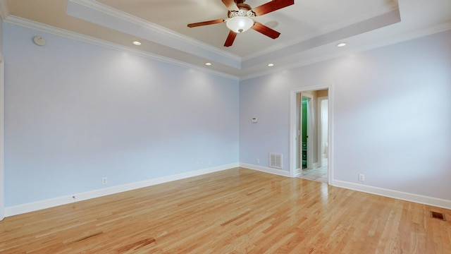 spare room with light wood finished floors, visible vents, baseboards, a raised ceiling, and ornamental molding