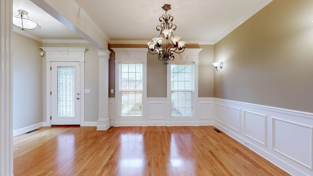 interior space with light wood-type flooring, ornate columns, crown molding, and a notable chandelier