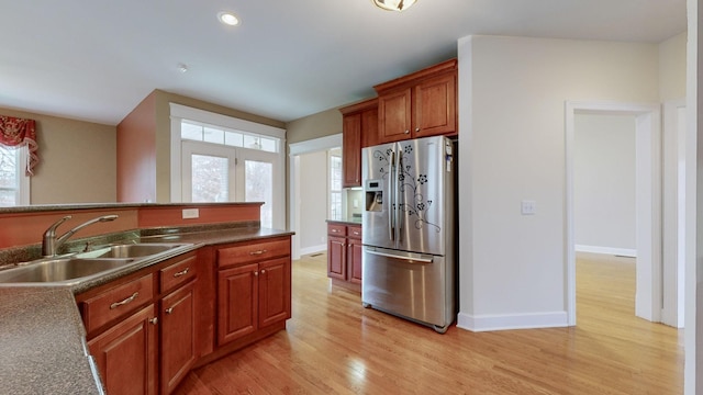 kitchen featuring a sink, baseboards, light wood-style floors, dark countertops, and stainless steel fridge