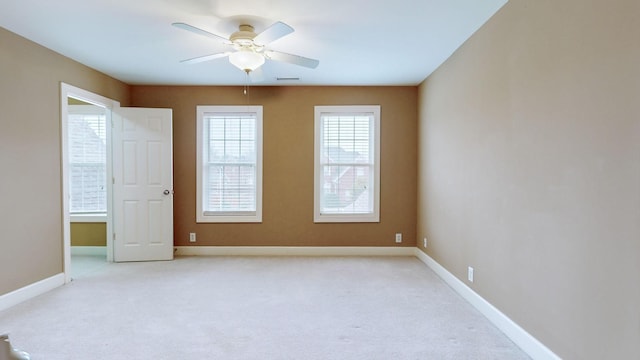 unfurnished room with a ceiling fan, light colored carpet, visible vents, and baseboards