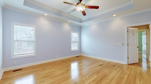 spare room featuring a tray ceiling, light wood-type flooring, visible vents, and baseboards