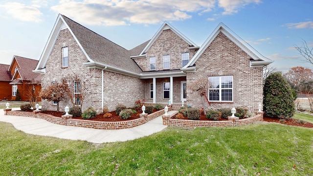 view of front of property with roof with shingles, brick siding, and a front lawn