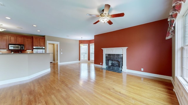 unfurnished living room with light wood-style flooring, recessed lighting, a fireplace, a ceiling fan, and baseboards