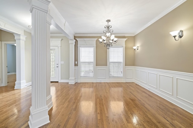 unfurnished dining area with ornate columns, crown molding, light wood-style floors, and wainscoting