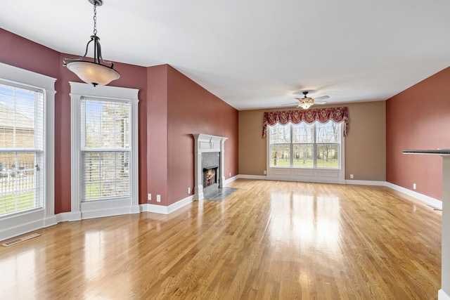 unfurnished living room with visible vents, baseboards, a ceiling fan, light wood-style flooring, and a fireplace