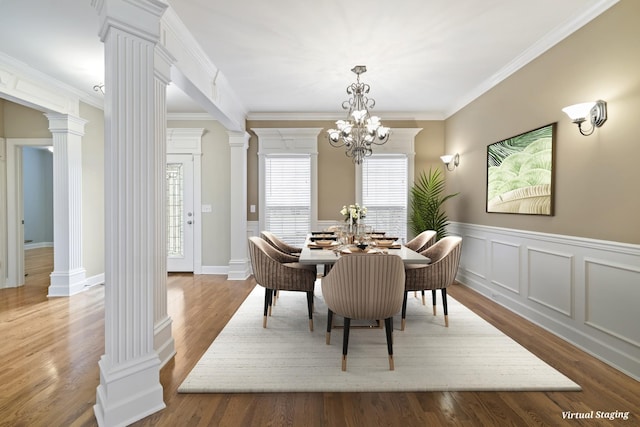 dining area featuring ornamental molding, wainscoting, wood finished floors, and decorative columns