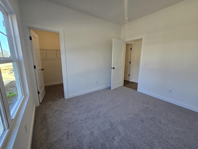 unfurnished bedroom featuring a walk in closet, dark carpet, and a closet