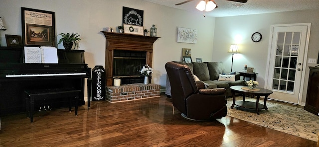 living area featuring ceiling fan, a fireplace, dark hardwood / wood-style flooring, and a textured ceiling