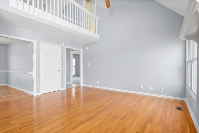 unfurnished living room featuring a towering ceiling, ceiling fan, and light wood-type flooring