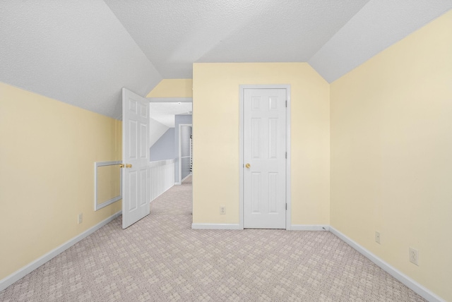 additional living space with vaulted ceiling, light colored carpet, and a textured ceiling