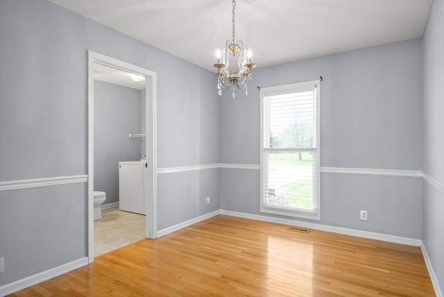 unfurnished room with wood-type flooring, washer / dryer, a textured ceiling, and a chandelier