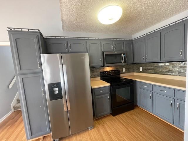 kitchen featuring decorative backsplash, stainless steel appliances, a textured ceiling, and light wood-type flooring