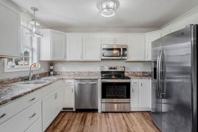 kitchen with white cabinets, hanging light fixtures, sink, appliances with stainless steel finishes, and wood-type flooring