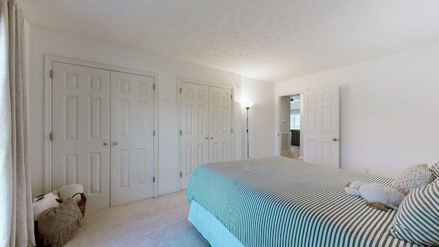 carpeted bedroom with a textured ceiling and multiple closets