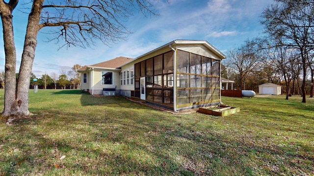 rear view of property featuring a yard, a sunroom, and an outbuilding